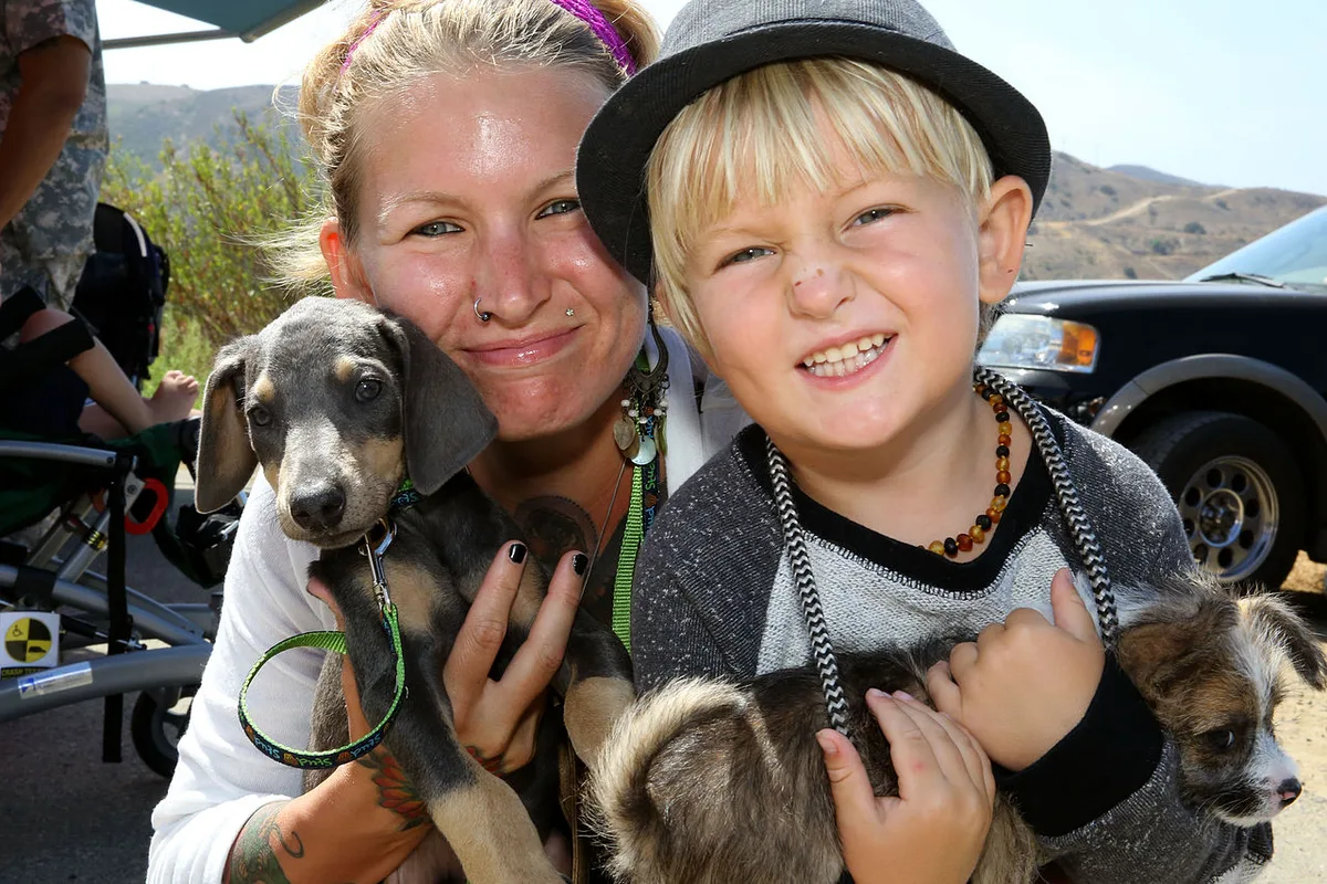 Een vrouw en een jongen houden ieder een pup vast op een adoptiedag.