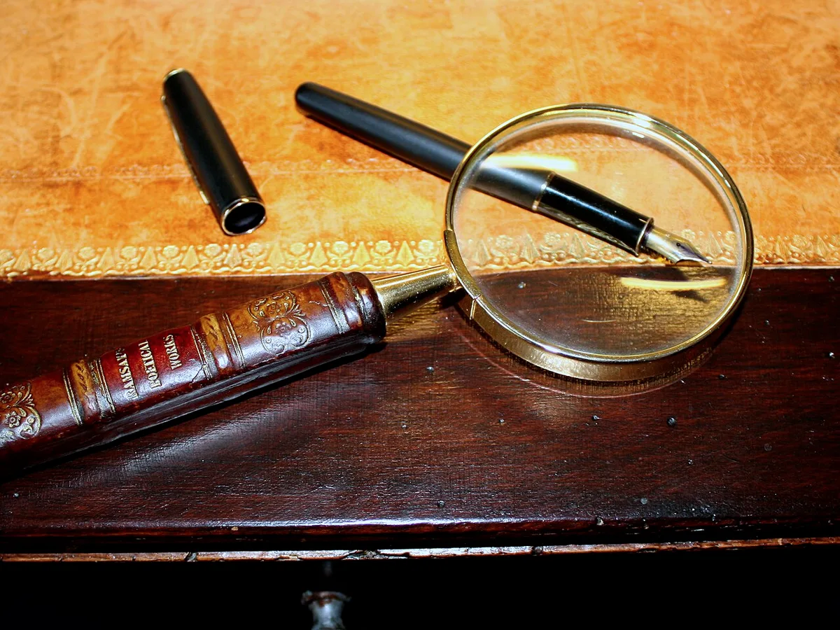 Een vergrootglas en een vulpen liggen op een houten bureaublad.